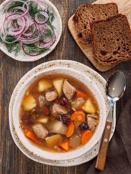 Clear soup with pork, potato, carrot and rosehip. Traditional russian siberian baikal soup yushka with meat. Perfect authentic delicious clear broth soup in rustic style on brown wooden background.