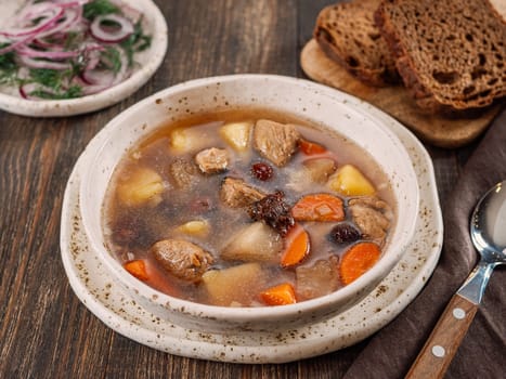 Clear soup with pork, potato, carrot and rosehip. Traditional russian siberian baikal soup yushka with meat. Perfect authentic delicious clear broth soup in rustic style on brown wooden background.