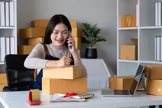 Startup SME small business entrepreneur SME or freelance Asian woman using a laptop with box, online marketing packaging box and delivery, SME concept..