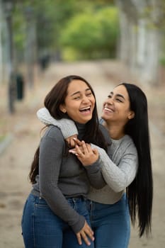 Happy lesbian latin females having fun together outdoors walking in a park.