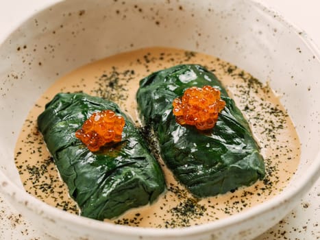 Stuffed green cabbage rolls with sauce in restaurant-style plating, served red caviar