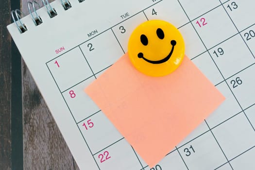 Orange paper sticky note with smiley face and stuck to a calendar background. Reminder concept. Copy space.