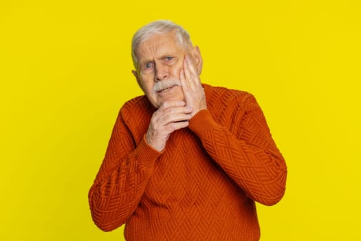 Dental problems. Senior old man touching cheek, closing eyes with expression of terrible suffer from painful toothache, sensitive teeth, cavities. Elderly grandfather pensioner on yellow background