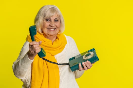 Hey you, call me back. Senior old woman talking on wired landline vintage telephone of 80s, advertising proposition of conversation, online shopping, hotline. Mature grandmother on yellow background