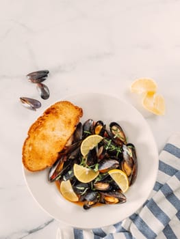 cooked mussels with lemon on white plate. Restaurant-style seafood plating. Seafood and mossels food background. Top view, copy space, vertical