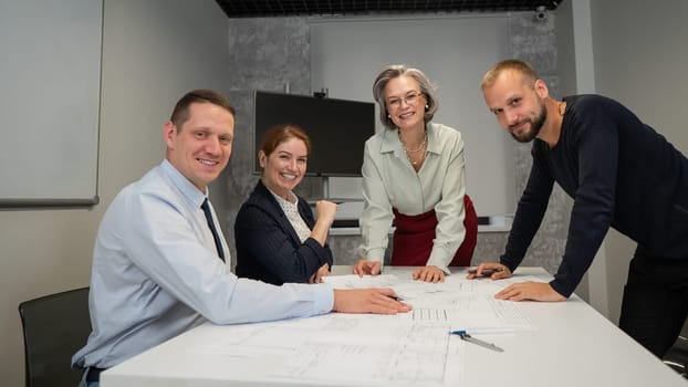 Designers engineers at a meeting discuss working drawings. Four smiling business people are looking at the camera
