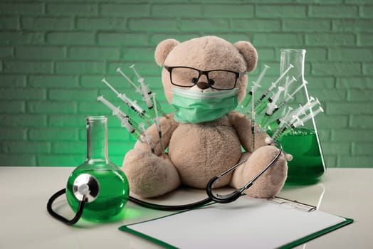 a teddy bear in a medical mask with syringes in his shoulder as a symbol of the research of vaccines and other drugs on animals or people