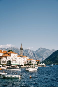 Excursion boats are moored off the coast of Perast with ancient houses and a church bell tower. Montenegro. High quality photo