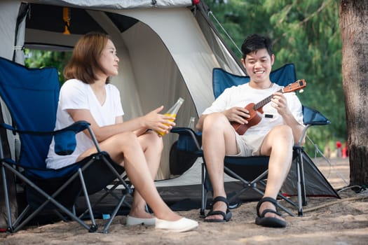 Camping bliss, A cheerful Asian couple, by their tent, serenades each other with ukulele tunes, spreading love and smiles under the setting sun. Togetherness is their melody. Camping outdoor