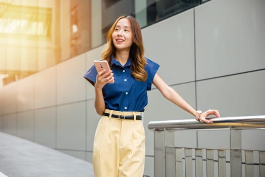 Woman with blue shirt using smartphone in the city. Busy young girl typing message on cell phone while walking on a sunny day.