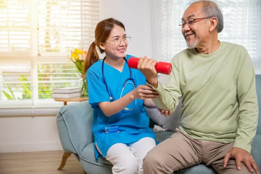 Young nurse physiotherapist helping old man in lifting dumbell at home, Asia nurse support elderly retirement sitting on sofa using red dumbbell workout exercise physical recovery, Health care concept