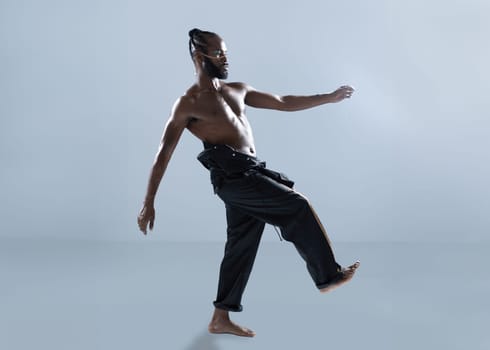 Barefoot shirtless african-american gay walk isolated on blue background, Gay African muscular macho man wearing make-up walking side view. Equality concept.