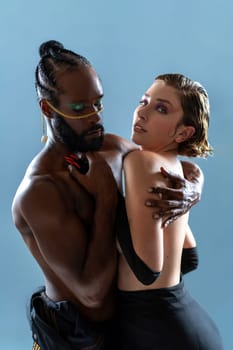 Life is beautiful with your partner by your side. Studio shot of two LGBT people hugging in dance pose. Black gay man wearing bright blue make up holding girlfriend dancing isolated on blue background