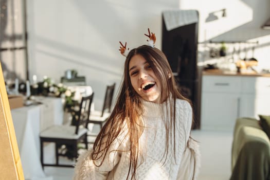 In the brightness of her apartment, a lively young woman wears a Christmas reindeer mask. High quality photo