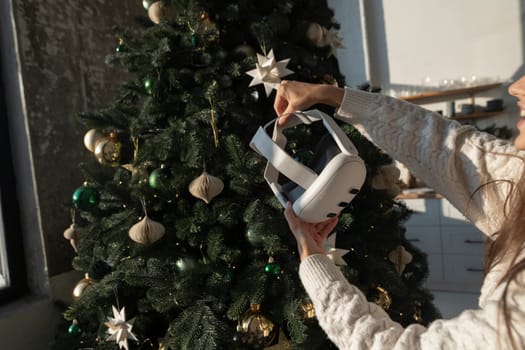 With the backdrop of a Christmas tree, a girl holds a virtual reality headset. High quality photo