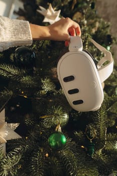 Against the scene of a Christmas tree, a girl holds a virtual reality headset. High quality photo