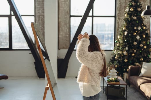 A vibrant young woman styling her hair for a Christmas party in front of the mirror at home. High quality photo