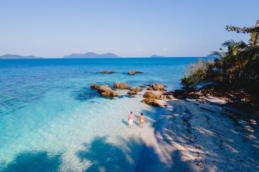 Drone aerial view at Koh Wai Island Trat Thailand. A young couple of men and women walking on a tropical beach during a luxury vacation in Thailand with a turqouse colored ocean