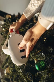 In front of a Christmas tree, a girl is holding a virtual reality headset. High quality photo