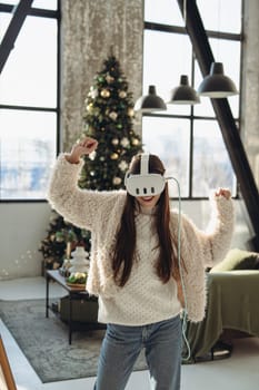 With a Christmas tree in the background, a lovely young woman explores virtual reality. High quality photo
