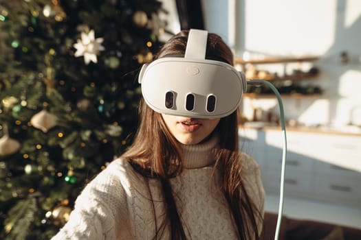 An image of a lovely girl wearing a virtual reality headset against the background of a Christmas tree. High quality photo