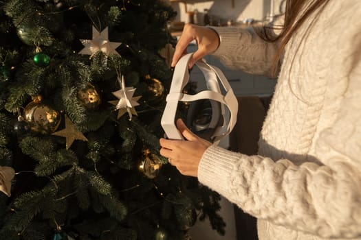With the backdrop of a Christmas tree, a girl holds a virtual reality headset. High quality photo
