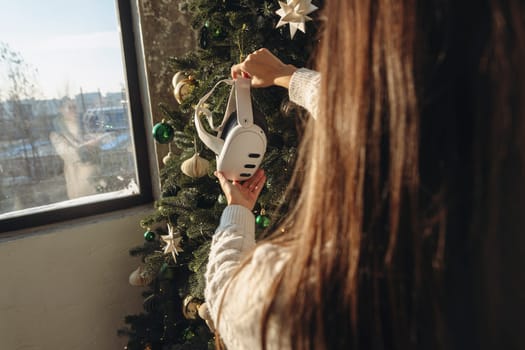 A girl holds a virtual reality headset against the backdrop of a Christmas tree. High quality photo