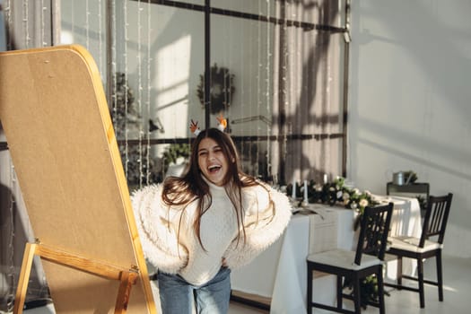 A bright young woman wearing a Christmas reindeer mask smiles cheerfully in an apartment. High quality photo