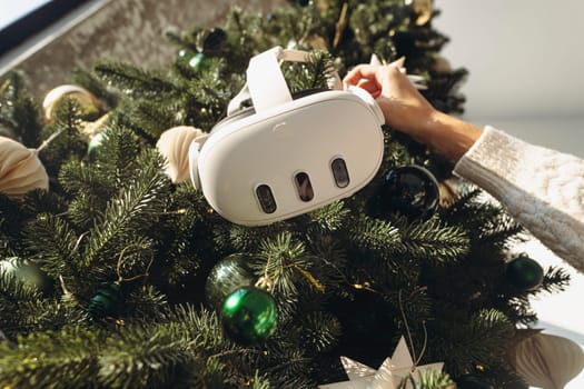 A girl holds a virtual reality headset against the backdrop of a Christmas tree. High quality photo
