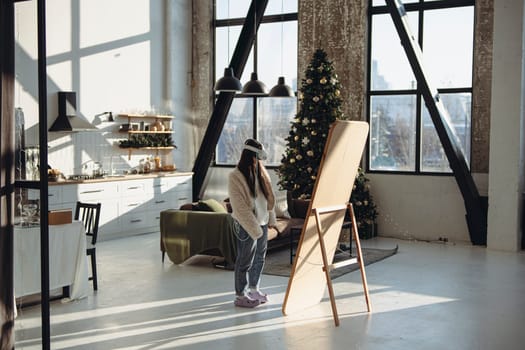 Surrounded by Christmas vibes, a young woman in light attire and a VR headset stands before the mirror. High quality photo