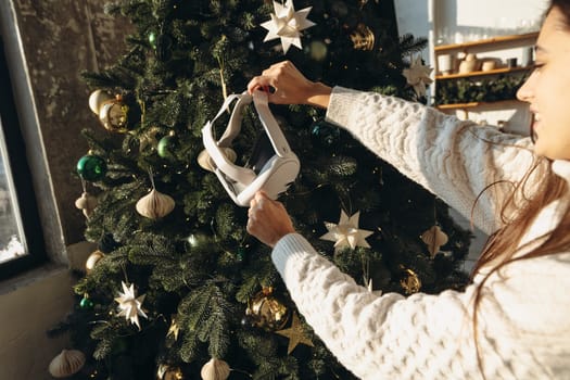 A girl, framed by a Christmas tree, holds a virtual reality headset. High quality photo