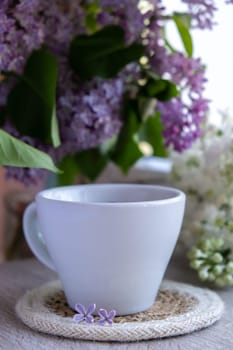 Tasty black tea in white cup on windowsill with aromatic lilac flowers. Spring composition Cup of lilac tea drinking recipe flowering branches of purple lilac. Still life for copy space greeting card, poster, banner, wallpaper. Relaxation and natural ingredients