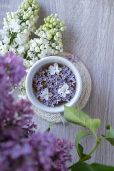 Tasty black tea in white cup on windowsill with aromatic lilac flowers. Spring composition Cup of lilac tea drinking recipe flowering branches of purple lilac. Still life for copy space greeting card, poster, banner, wallpaper. Relaxation and natural ingredients