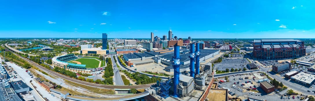 2023 Aerial panorama of Indianapolis, showcasing its iconic skyline, Lucas Oil Stadium, Perry K. Generating Station, and serene river, under a clear blue sky