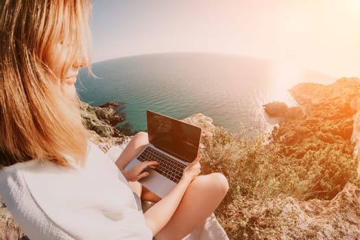 Woman sea laptop. Business woman in yellow hat working on laptop by sea. Close up on hands of pretty lady typing on computer outdoors summer day. Freelance, digital nomad, travel and holidays concept.