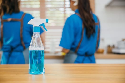 Occupied woman cleaning kitchen desk using spray product and towel. Housekeeping concept with a focus on hygiene and safety. Uniformed cleaner at work. Clean disinfect home care. Closeup spray bottle.