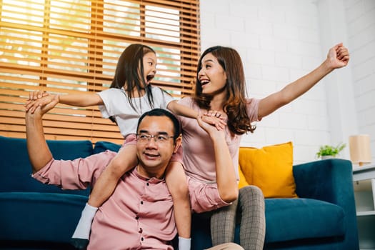 A happy Asian family father mother and daughter share affectionate moments on a comfortable sofa in their modern house embracing togetherness during self-isolation.
