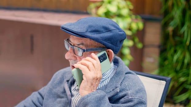 Photo of a senior man wearing beret talking to the mobile sitting outdoors a geriatric