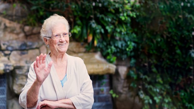 Photo with copy space of a grandmother waving and smiling in a garden