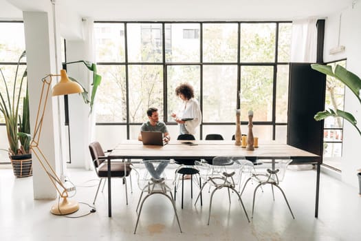 Young multiracial people interacting in spacious bright co working office with big window. Coworkers. Copy space.