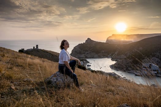 Happy woman on sunset in mountains. Woman siting with her back on the sunset in nature in summer. Silhouette