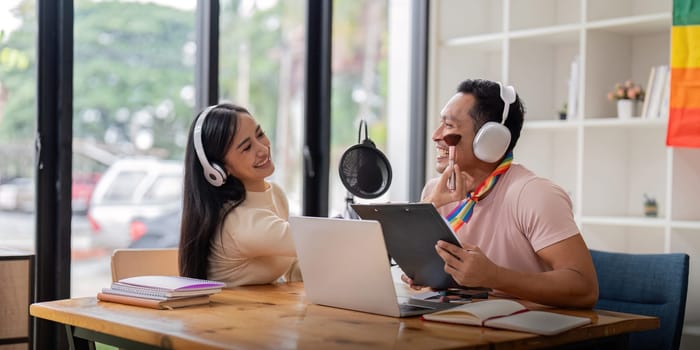 Young gay man and girl friend using laptop and microphone streaming audio podcast at studio.