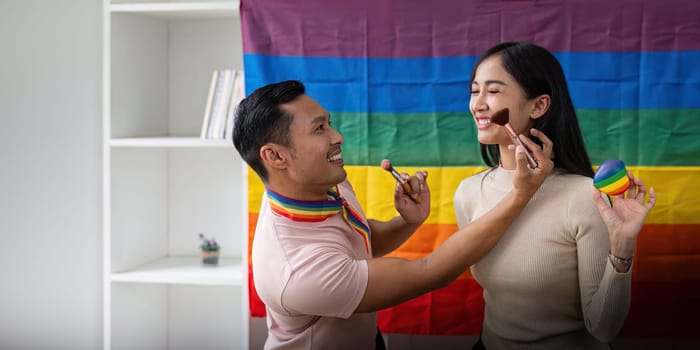 Playful gay male applying makeup with brush on face young woman friend together.