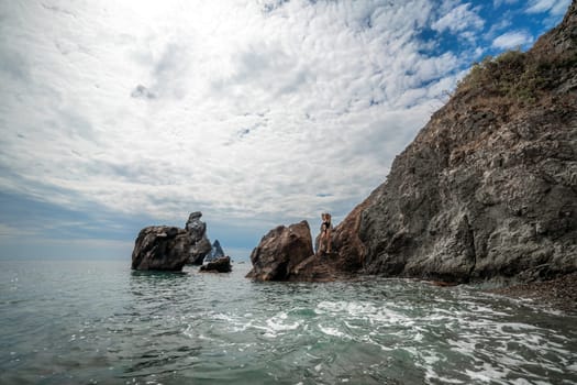 Woman swimsuit sea. Attractive blonde woman in a black swimsuit enjoying the sea air on the seashore around the rocks. Travel and vacation concept