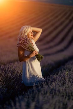 Blonde woman poses in lavender field at sunset. Happy woman in white dress holds lavender bouquet. Aromatherapy concept, lavender oil, photo session in lavender.