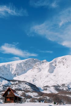 Brown wooden two-story cottage in a mountain village at the foot of the snow-capped mountains. High quality photo