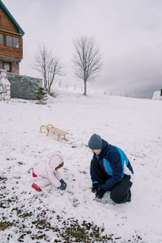Dad and a little girl are squatting on a hill near a sled and making snowballs. High quality photo