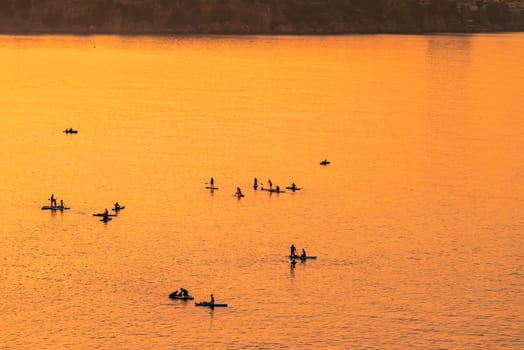 Adventurous people on a stand up paddle board is paddling during a bright and vibrant sunrise