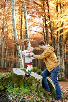 Dad holding hands a little girl walking on the stumps in the autumn park. High quality photo