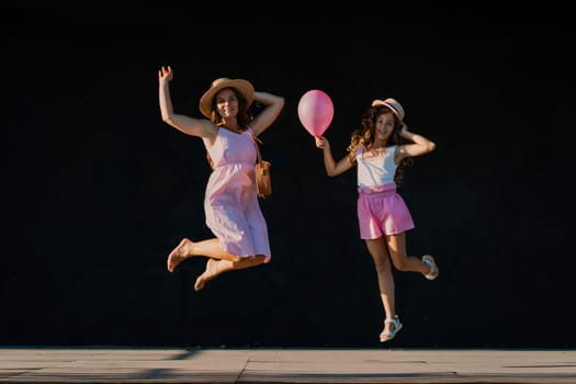 mother and daughter jumping in pink dresses with loose long hair on a black background. Enjoy communicating with each other.